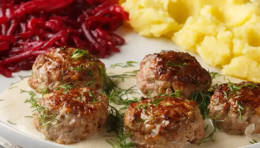 Pięć soczystych klopsów w kremowym sosie, udekorowanych koperkiem, podanych z purée ziemniaczanym i buraczkami.