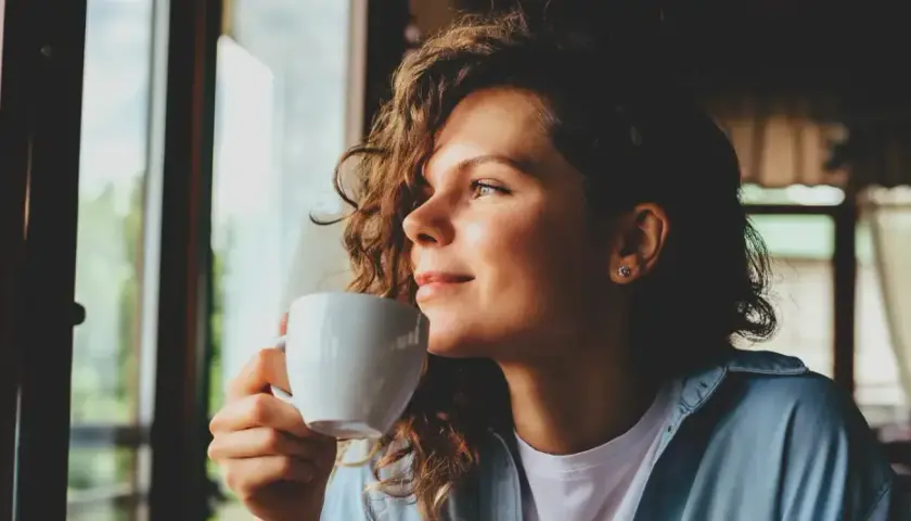 Frau mit lockigen Haaren genießt eine Tasse Chai Latte, ein Moment der Ruhe während der Schwangerschaft.