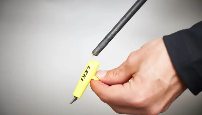 Hand hält gelbes Werkzeug mit "LEKI" Schriftzug, um die Spitze eines Skistocks zu wechseln.