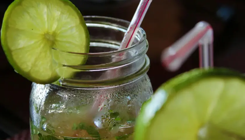 Orzeźwiający mohito drink, z widocznymi składnikami: limonką i miętą, w szklanym słoiku z rurką.