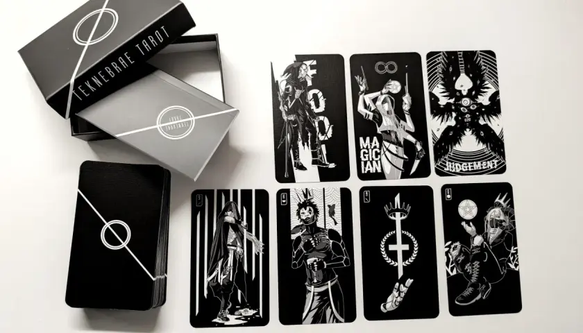 Czarno-białe karty z talii tarot z 5 kartami, w tym Mag, Sąd i inne postacie. Pudełko z napisem "TEKNEBRAE TAROT".