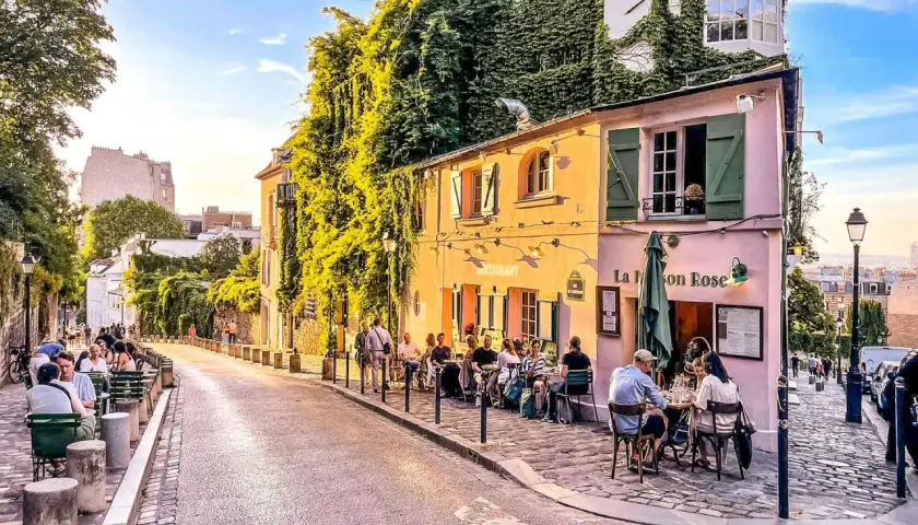 Ulica na Montmartre, z kawiarnią La Maison Rose i ludźmi siedzącymi przy stolikach.