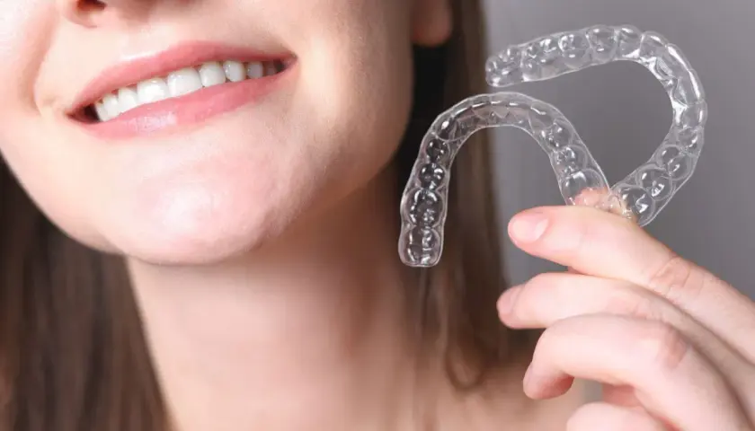Una persona sonríe mostrando sus dientes y sostiene un alineador transparente. Invisalign para que sirve: para corregir la alineación dental de forma discreta.
