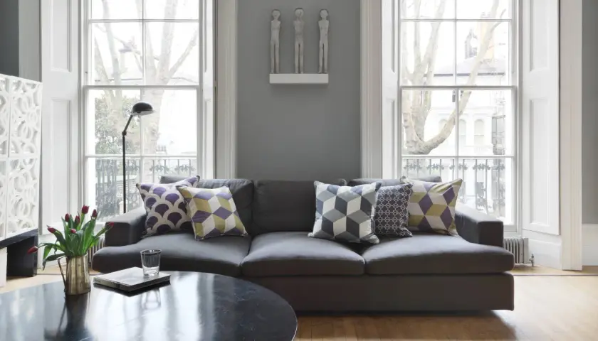Graues Sofa mit Kissen in Lila, Gelb und Grau. Die Farben passen gut zu Grau und schaffen eine gemütliche Atmosphäre.