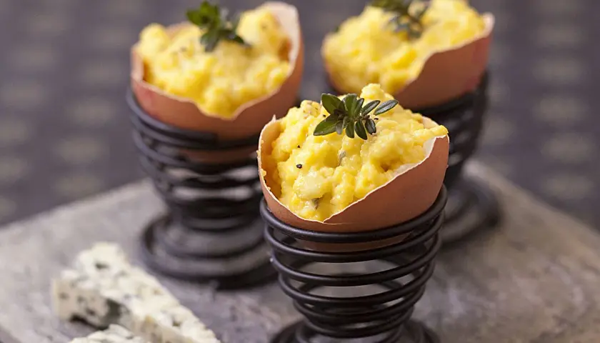 Une entrée pour Pâques avec des œufs farcis, garnie d'herbes fraîches. Du fromage bleu est disposé à côté.
