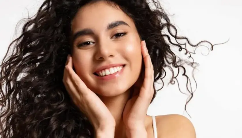 Sonrisa radiante con un toque de strawberry makeup, cabello rizado oscuro y piel luminosa.