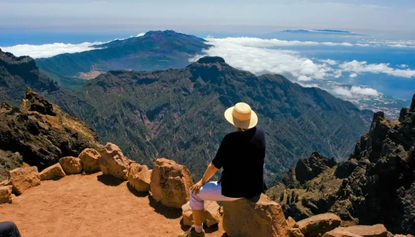 Persona con sombrero admira el paisaje montañoso y el mar, disfrutando de las **rutas La Palma**.