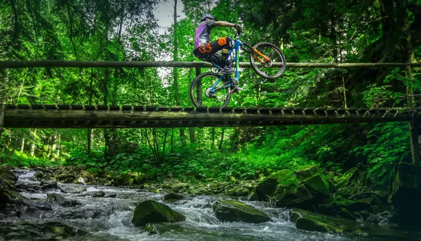 Rowerzysta wykonuje trik na drewnianym moście nad potokiem. Wspaniałe **trasy rowerowe Zakopane** czekają na odkrycie!