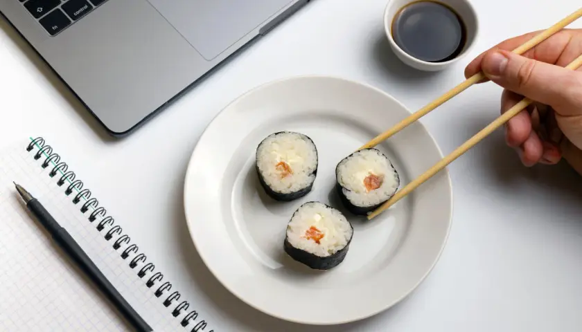 Praca i zdrowie idą w parze. Na biurku laptop, notatnik i pałeczki do sushi, idealne dla zwolenników peskatarianizmu.