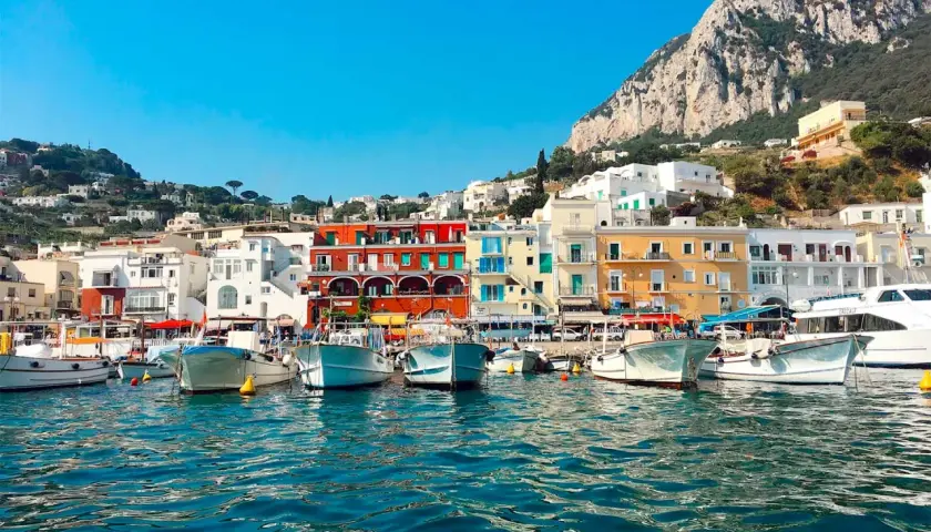 Vue du port de Capri, avec des bateaux blancs amarrés et des maisons colorées à flanc de colline. Un paysage typique de Capri, pas Ischia.