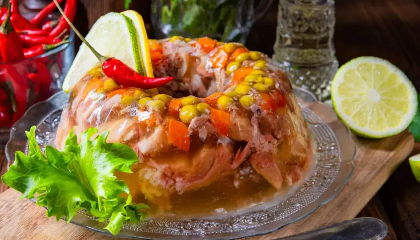 Garmażerka w galarecie, ozdobiona papryczką chili, cytryną i zieloną sałatą, wygląda apetycznie.