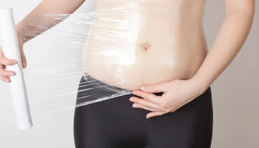 Osoba owija brzuch folią spożywczą, próbując dowiedzieć się, body wrapping co to jest i jak działa.