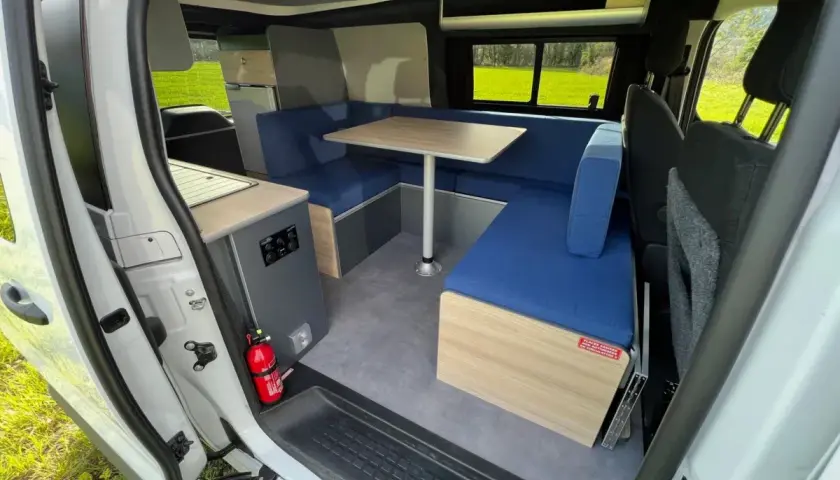 Aménagement intérieur d'un camping-car : banquettes bleues, table, coin cuisine. Idéal pour construire son camping car.