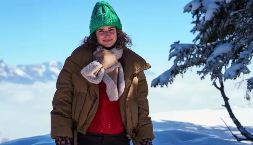 Frau mit grüner Strickmütze und brauner Winterjacke im Schnee.