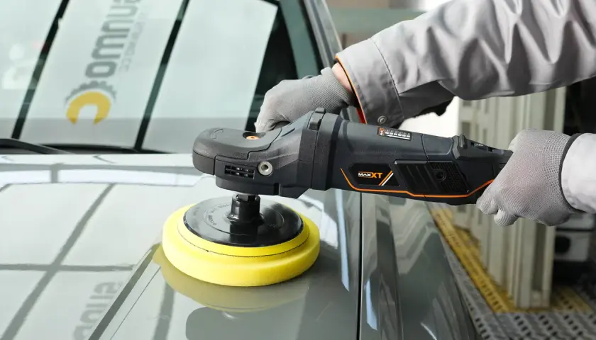 Persona con guantes usa una pulidora para detallar el capó de un coche gris.
