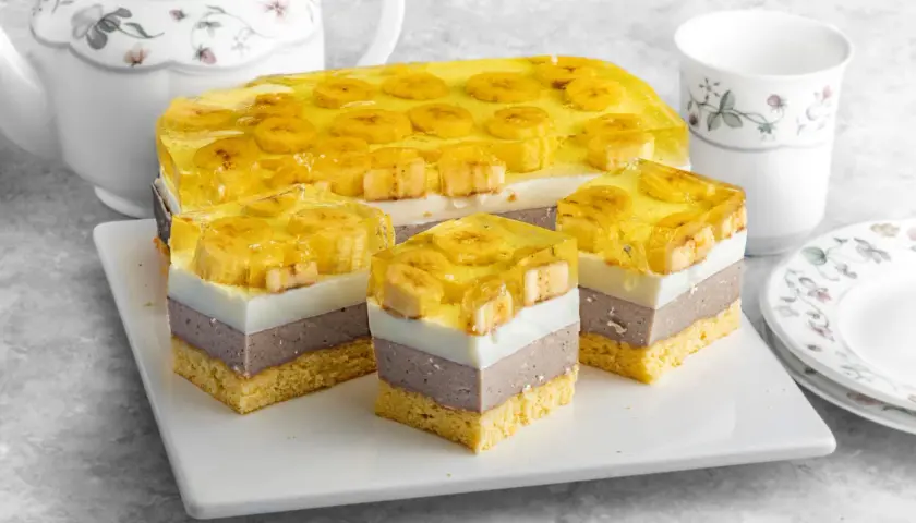 Pyszne bananowiec ciasto z galaretką i bananami, pokrojone na porcje. Obok czajniczek i filiżanka.