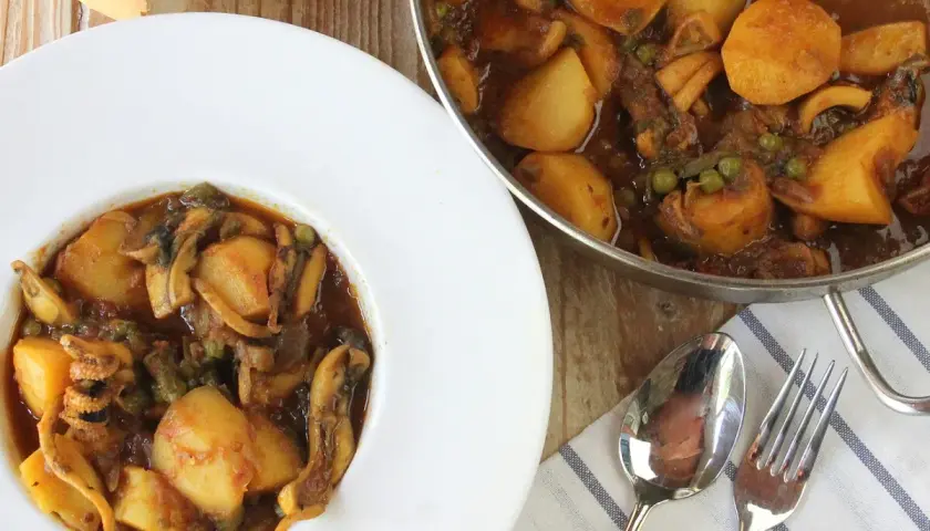 Un plato de papas con choco, un guiso casero con trozos de patata, calamares y guisantes en una salsa oscura.