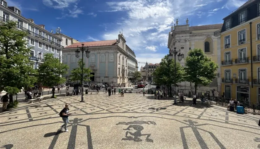 A sunny day trip to Lisbon, exploring a beautiful square with intricate mosaic paving and historic buildings under a blue, cloudy sky.