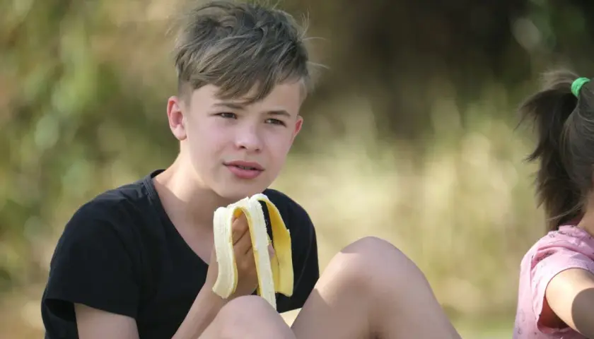 Chłopiec je banana. Zastanawia się, ile kalorii powinna jeść 13 latka, by mieć energię do zabawy.