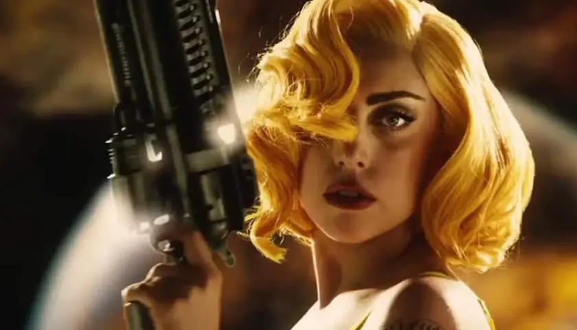 Lady Gaga med blont hår och en futuristisk pistol i en scen från en av hennes filmer.