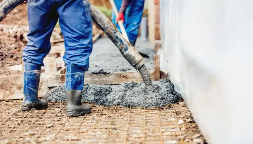 Pracownicy wylewają beton na zbrojenie. Sprawdź aktualny suchy beton cena 1m3.