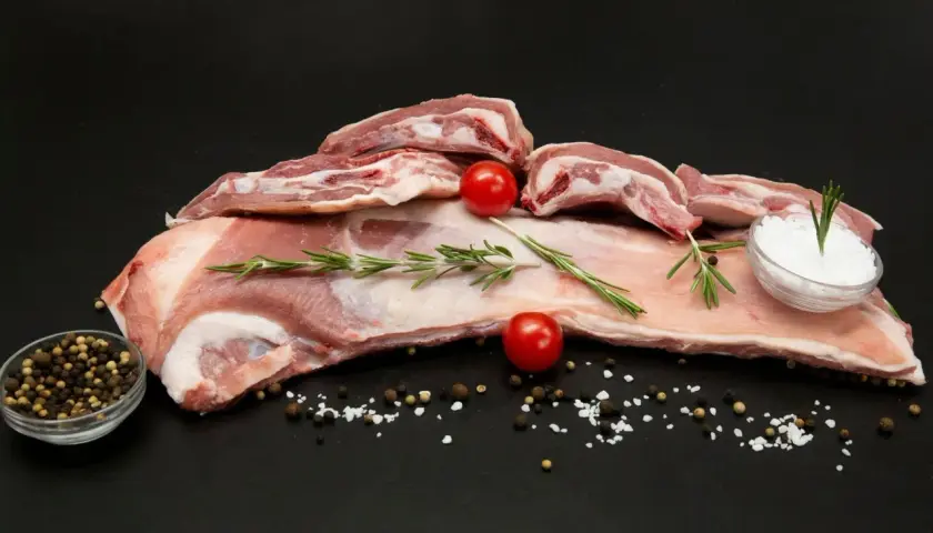Poitrine d'agneau crue, parsemée de sel, poivre, romarin et tomates cerises, prête à être cuisinée.