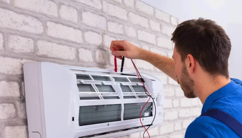 Technik sprawdza klimatyzator, który nie chłodzi. Używa multimetru do diagnozy problemu.