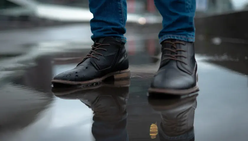 Man in jeans and black boots standing in a puddle. Learn how to rough up the bottom of slippery shoes for better grip.