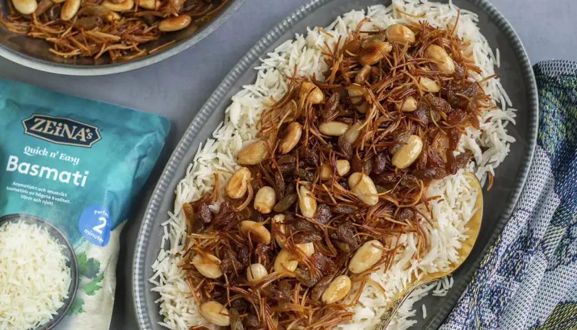 En tallrik med fluffigt basmatiris toppat med en blandning av stekt vermicelli, russin och mandlar. En påse Zeina's Quick n' Easy Basmati syns bredvid.