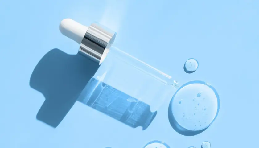 Droppe av serum med hyaluronsyra och retinol på blå bakgrund.