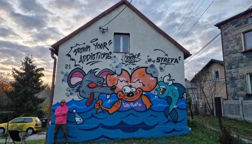 Kolorowy mural na domu jednorodzinnym przedstawia kreskówkowe zwierzęta w wodzie. Widać mysz, małpkę z napisem "LIFE GUARD" i rybę.