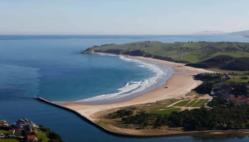 Impresionantes playas cerca de San Vicente de la Barquera, con olas rompiendo en la arena dorada y verdes colinas al fondo.