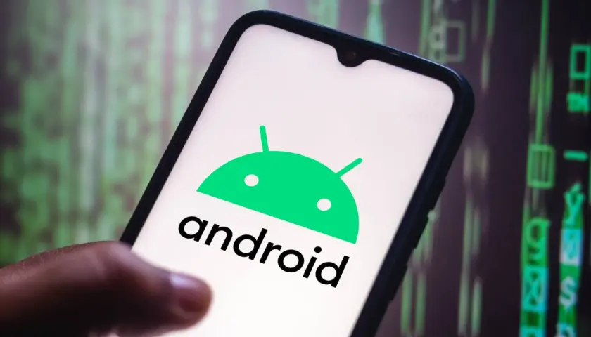 Dłoń trzyma smartfon z logo Android 10. W tle widać zielony, cyfrowy kod.