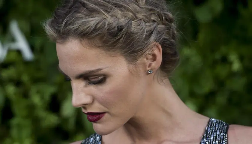 Mujer con elegante peinado con trenzas, maquillaje dramático y vestido brillante.