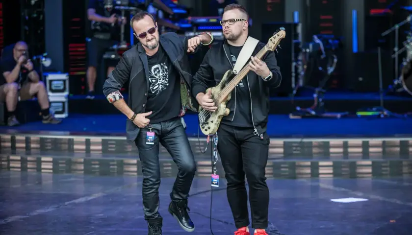 Dwóch muzyków na scenie, jeden z gitarą basową, drugi w okularach przeciwsłonecznych. Wyglądają jak nowy wokalista Kombi i jego kolega z zespołu.