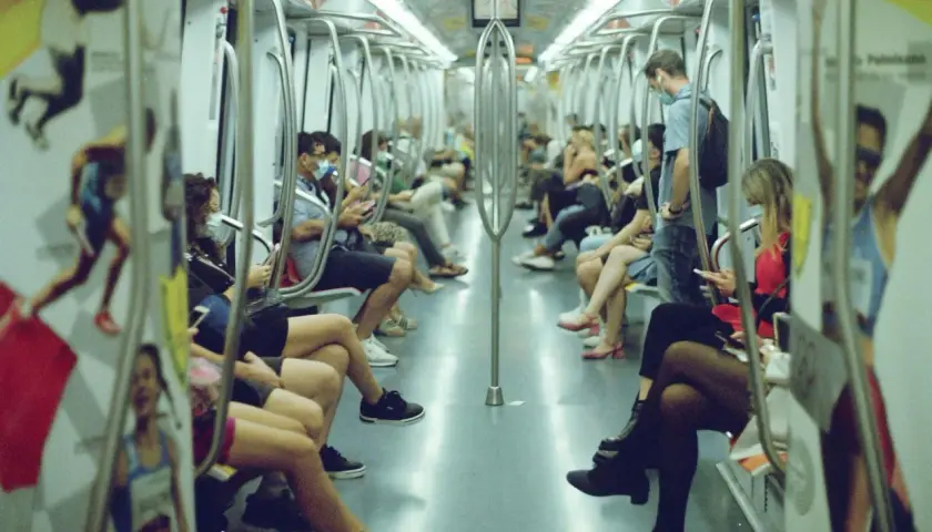 Interno di un vagone della metro di Roma, con passeggeri seduti e in piedi. L'orario del metro è visibile su un cartello.