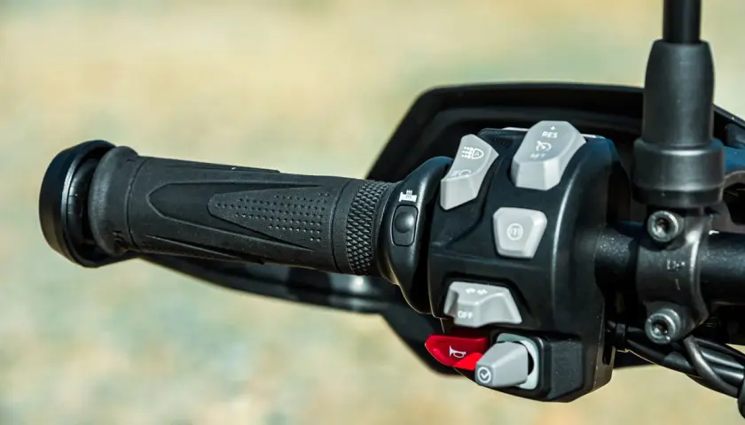 Mandos de la moto: puño negro texturizado y panel de control con botones grises y rojos para luces, crucero y bocina.