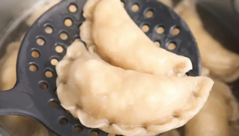 Gotowe pierogi z serem na łyżce cedzakowej, gotujące się w garnku. Idealne, by pokazać, jak zrobić pierogi z serem.