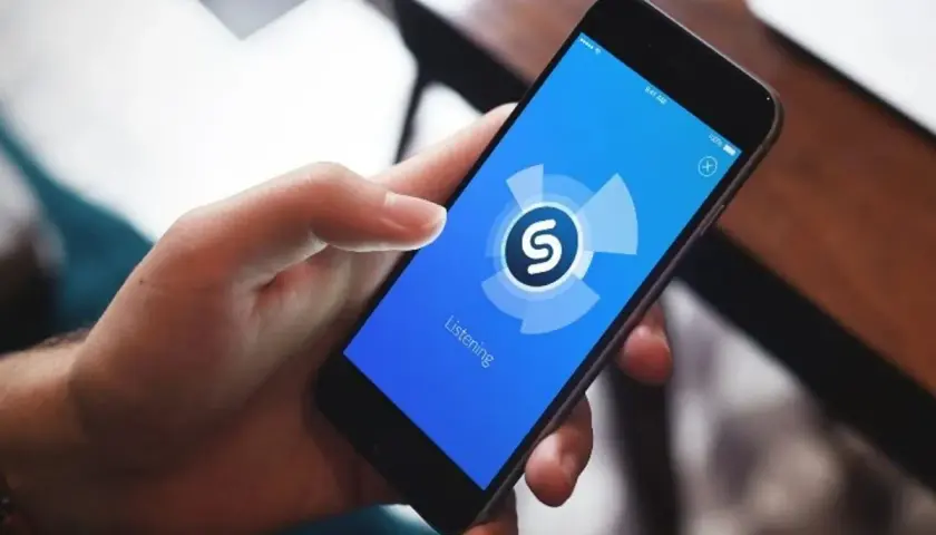 Dłoń trzyma smartfon z aplikacją Shazam, która analizuje dźwięk. Zastanawiasz się, jaka to piosenka?