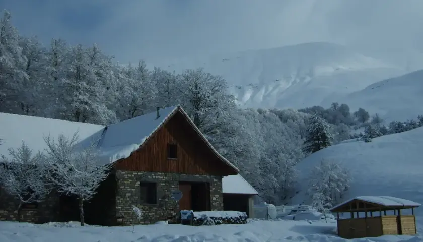 El refugio de Linza, cubierto de nieve, se alza entre árboles nevados y montañas imponentes.
