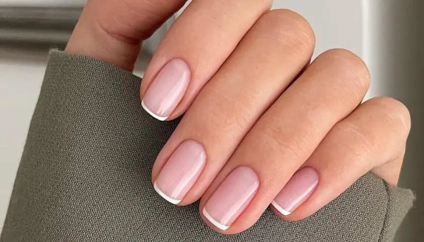 Dłoń z idealnie wykonanymi, eleganckimi paznokciami french. Delikatny róż i klasyczna biel tworzą ponadczasowy manicure.