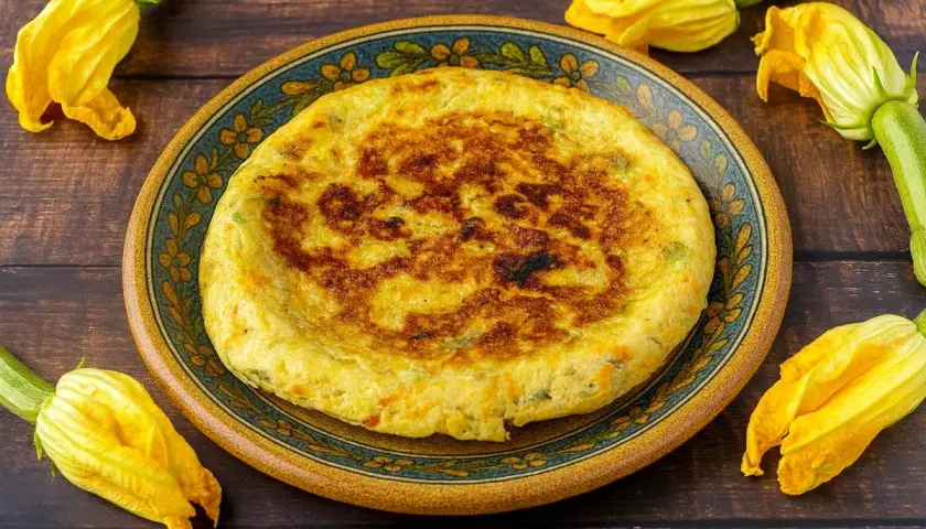 Frittata dorata con fiori di zucca, servita su un piatto decorato, circondata da fiori freschi.