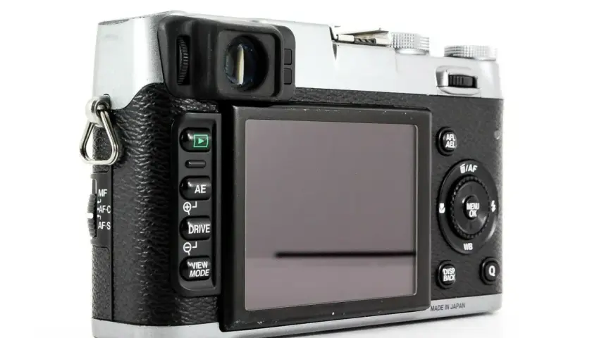 Tył aparatu Fujifilm X100S z widocznym ekranem, przyciskami sterującymi i pokrętłami.
