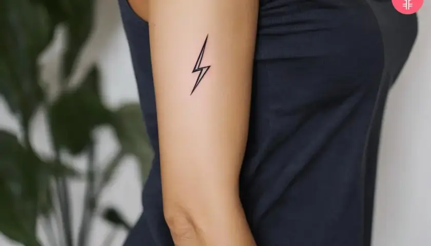 Minimalistyczny tatuaż piorun na ramieniu kobiety. Symbolizuje moc i energię.