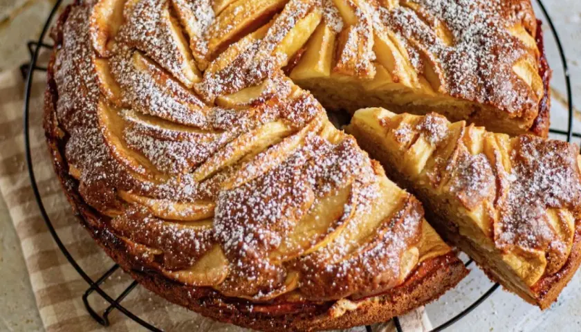 Un gâteau aux pommes et mascarpone irrésistible, saupoudré de sucre glace, avec une part coupée.