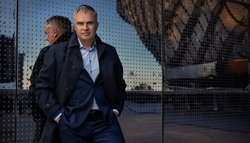 Jerker Virdborg står framför en reflekterande fasad, klädd i kostym och rock.