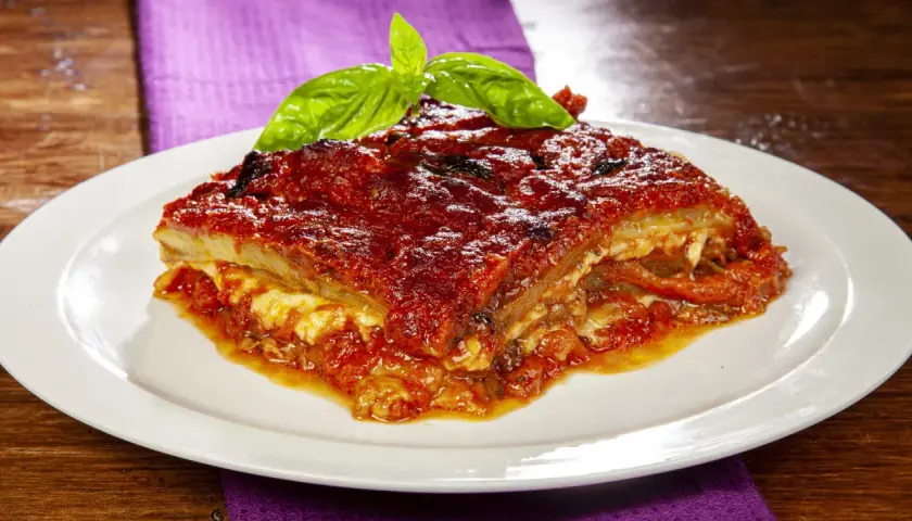 Una fetta di parmigiana di melanzane napoletana, ricca e saporita, guarnita con basilico fresco.