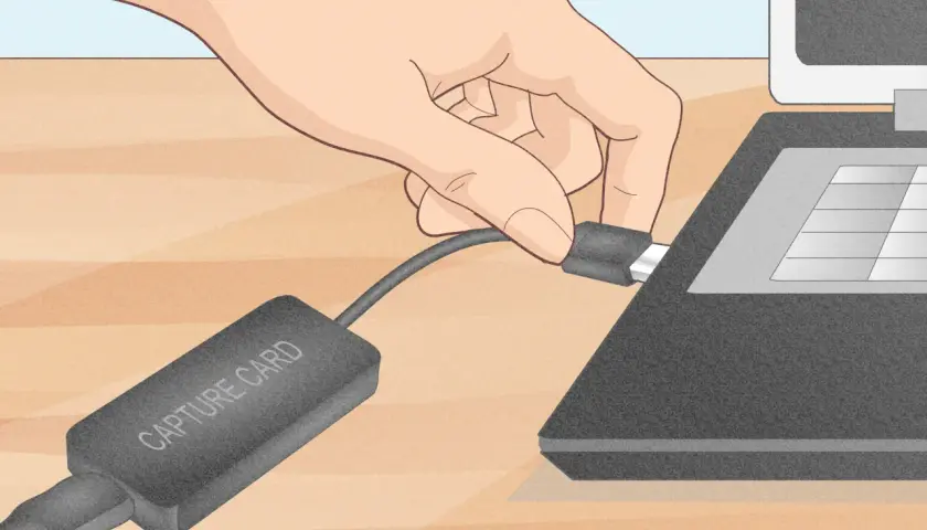 Dłoń podłącza kabel karty przechwytującej do laptopa.