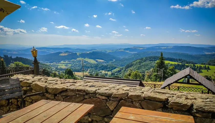 Widok z góry Sowa na malownicze wzgórza. Drewniane stoły i kamienny murek zapraszają do podziwiania panoramy.