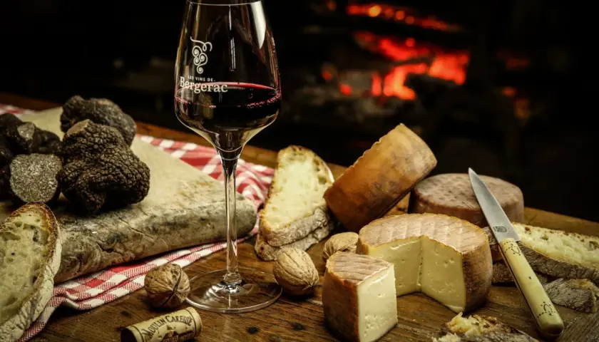 Verre de vin rouge, truffes noires, fromages et pain sur une table en bois, près d'une cheminée. Un délice pour accompagner un vin avec truffade.